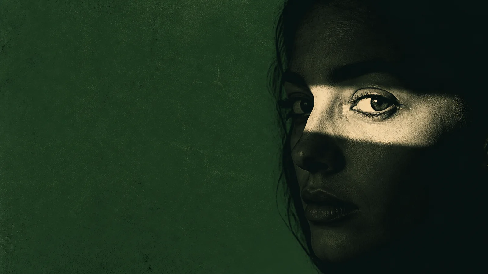 A face in deep green shadow with a narrow band of light across the eyes